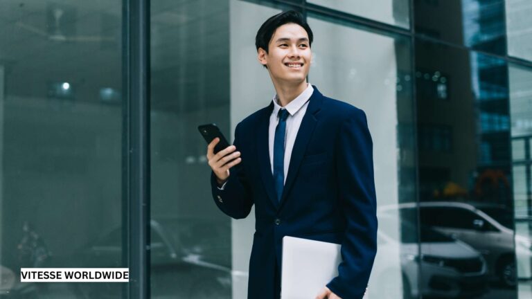 Businessman holding phone outside office building.